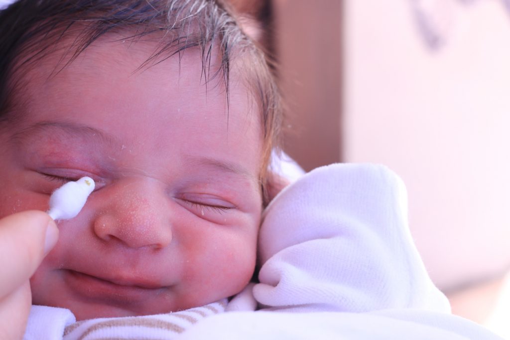 Mother cleaning sticky eyes of a newborn baby with cotton stick