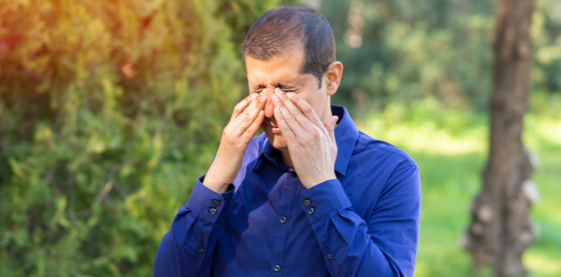Man rubbing irritated eyes while outdoors