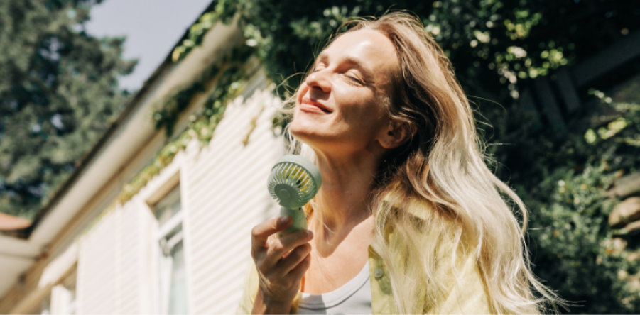 Woman using a handheld fan to cool herself outdoors in hot weather